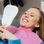 Oral health. Woman lying on her back, looking at her teeth in the mirror