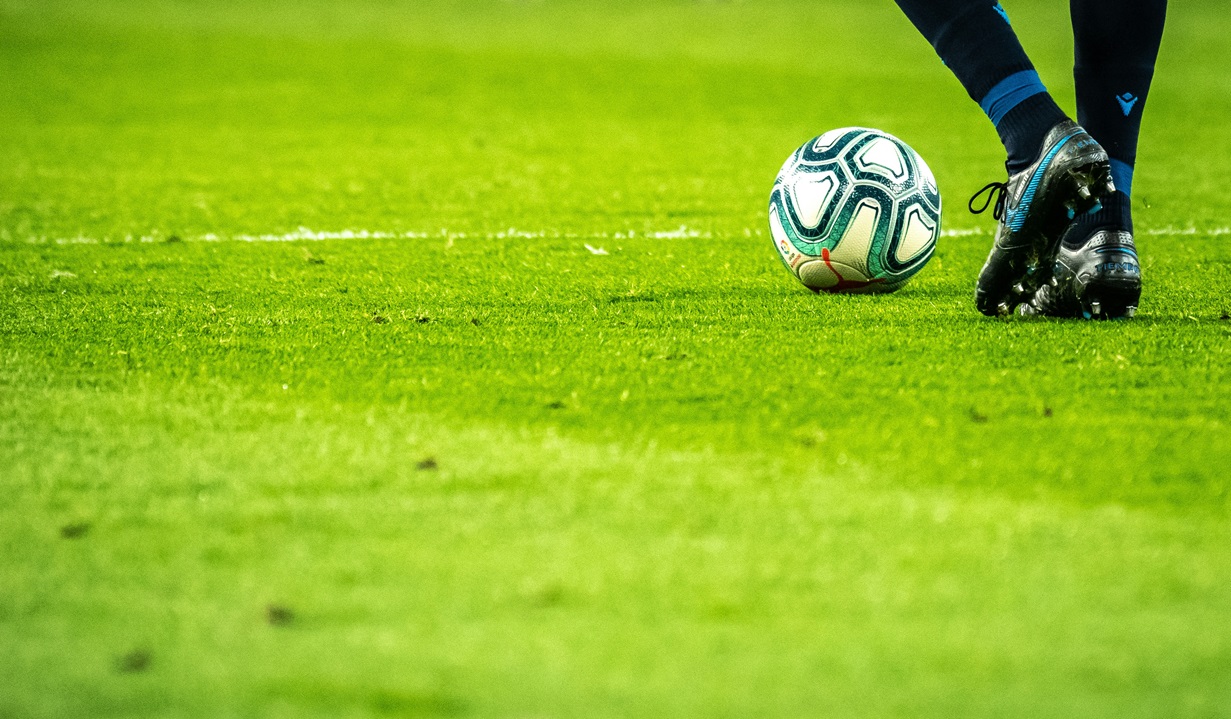 Soccer ball on green grass with the legs of a player