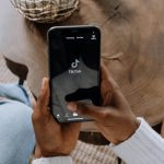 Hands holding a phone with TikTok on the screen. TikTok allows you to make money as a faceless brand