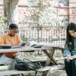 2 female students with earphones and books on a bench