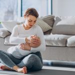 Young woman breast feeding toddler son and sitting on mat