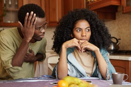 Sad disappointed woman can't forgive her husband for infidelity who is sitting next to her having apologetic guilty look, saying it was a mistake. African American couple facing relationships problems