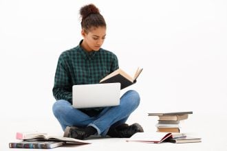 Portrait of young beautiful african girl with laptop and books reading over white background. Copy space.