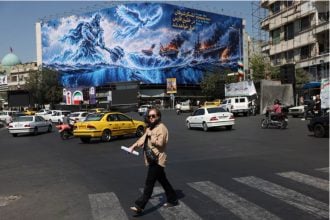 Woman walks past Strait of Hormuz billboard in Tehran amid Iran sanctions